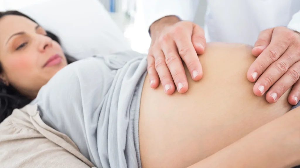 a pregnant woman lays down while a chiropractor's hands rest on her stomach