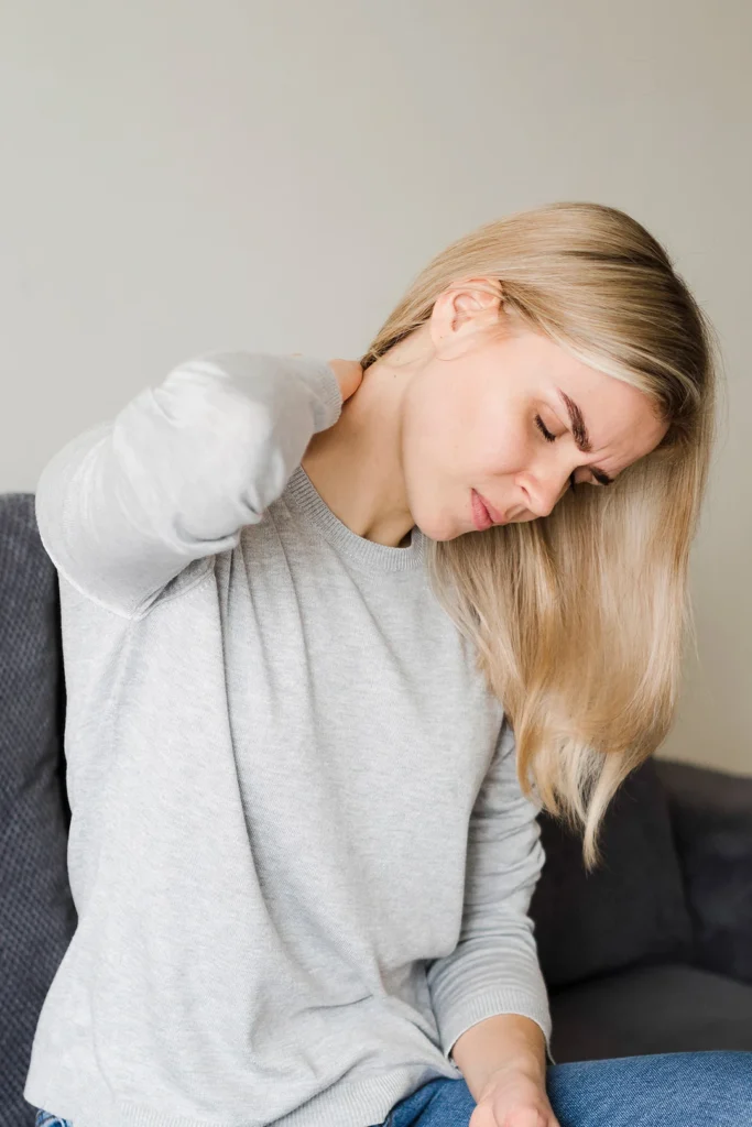 Woman Sitting On Couch Looking Down While Holding Neck In Pain